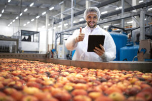 Technologist showing thumbs up in food processing factory and checking quality of apple fruit.